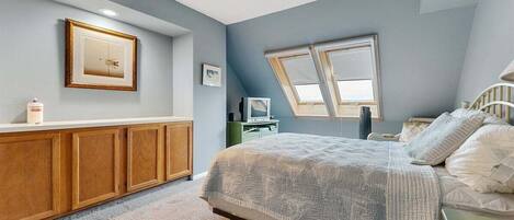 A bedroom with a bed, wooden cabinets, a television, and a window.