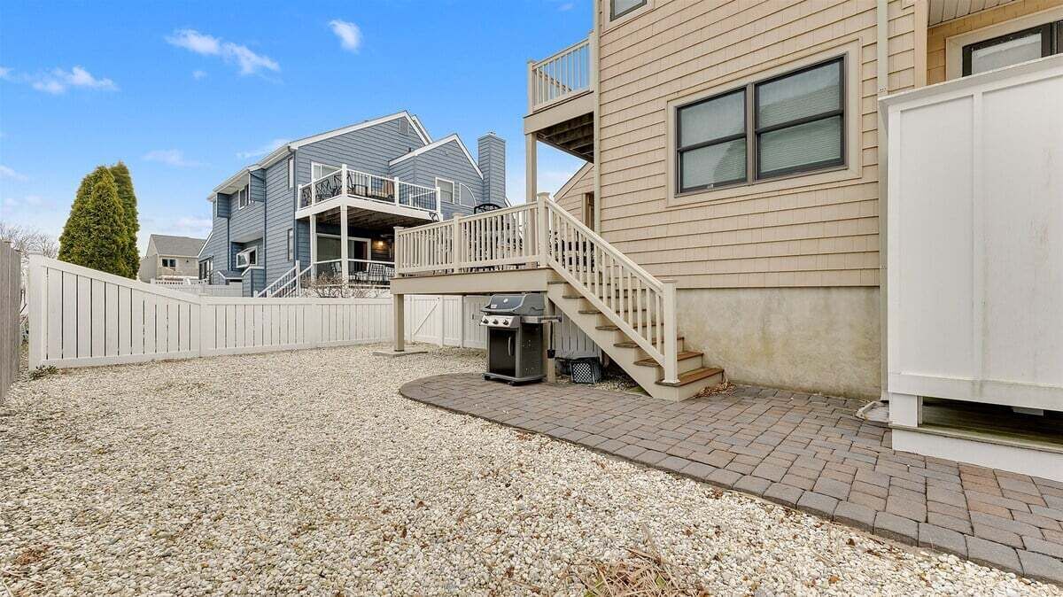 Un immeuble résidentiel avec une allée en gravier, un barbecue et une clôture blanche.