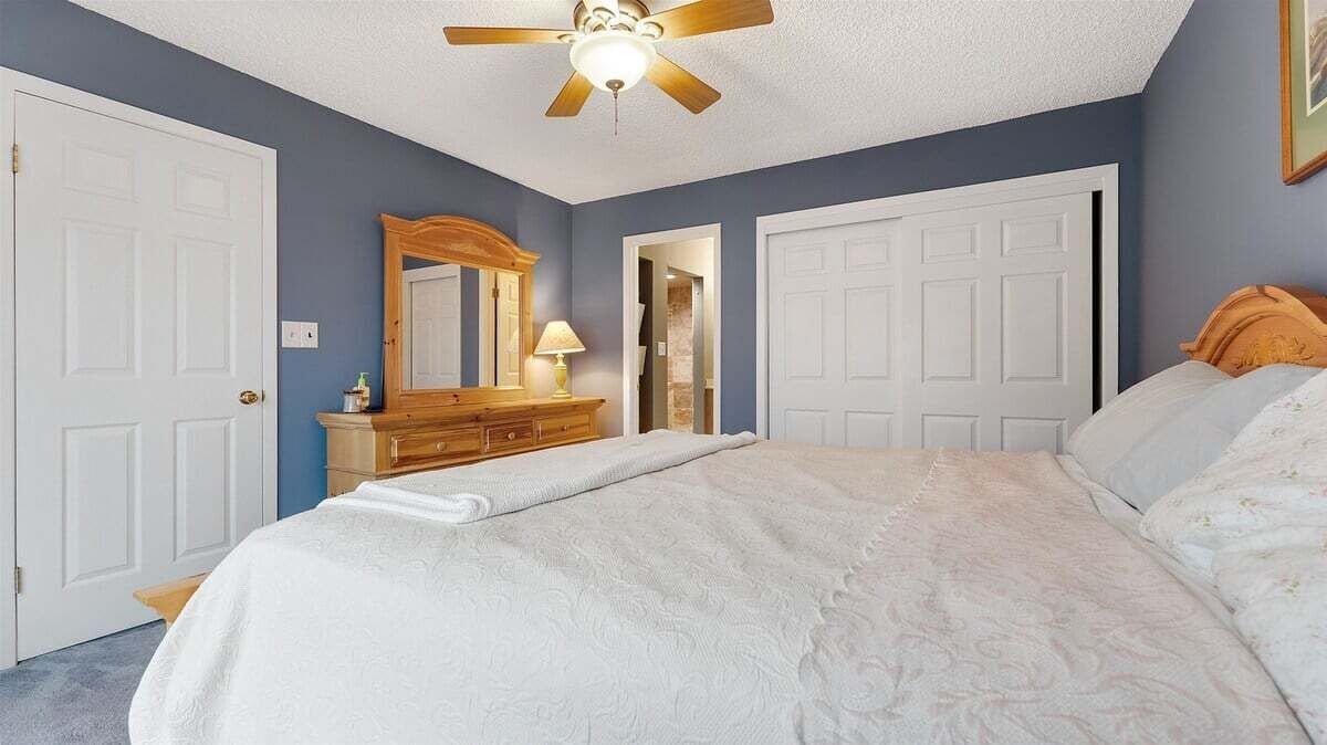 Une chambre à coucher comprenant un lit, une commode, un miroir, un ventilateur de plafond et deux portes.