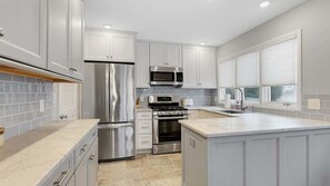 Une cuisine moderne dotée d’appareils électroménagers en acier inoxydable, de meubles blancs et d’un grand îlot central.