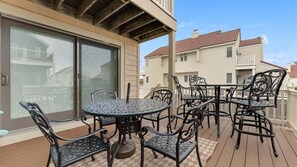 Eine überdachte Terrasse mit einem runden Tisch und Stühlen, einer Glasschiebetür und Blick auf benachbarte Gebäude.