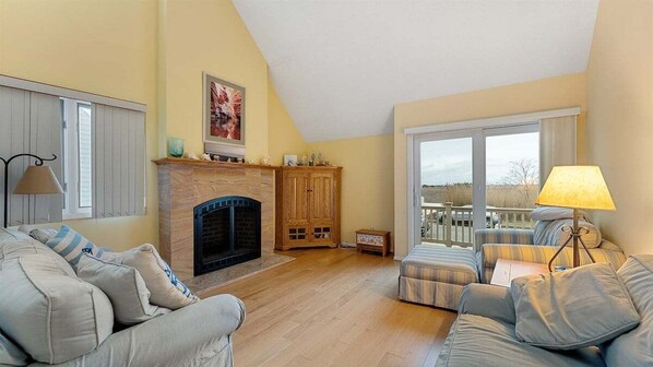 Ein Wohnzimmer mit Kamin, einer Couch, einer Lampe und Blick ins Freie.