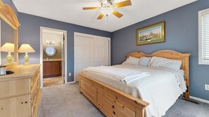 Ein Schlafzimmer mit einem hölzernen Bett, einem Deckenventilator, einem Schminktisch, einem Spiegel und einer Tür zu einem Badezimmer.