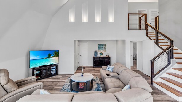 Een ruime woonkamer met een grote flatscreen-tv, een ronde salontafel en een beige hoekbank.
