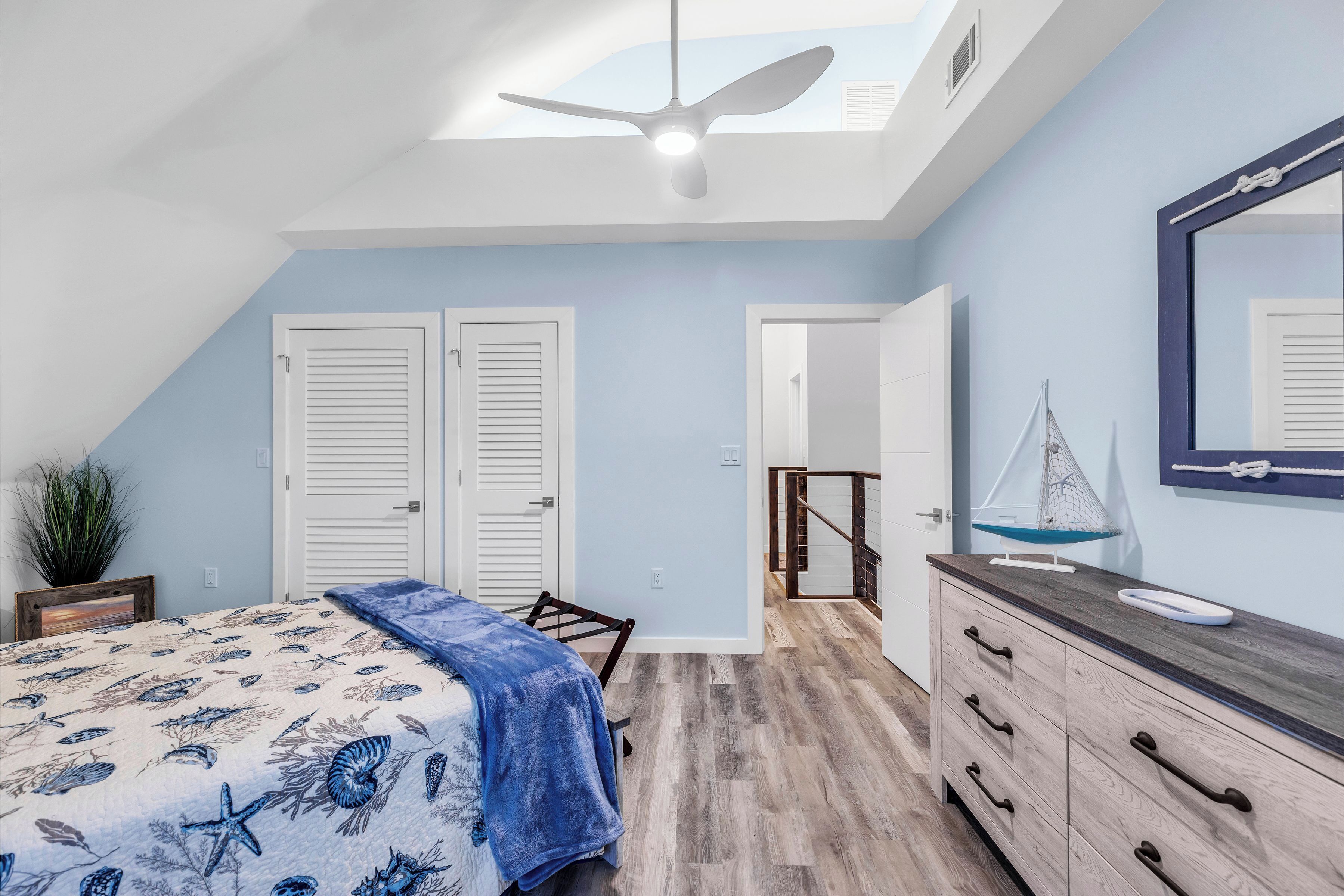 A bedroom with a bed, a dresser, a ceiling fan, and a skylight.
