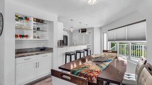 Een moderne keuken met witte kasten, een marmeren aanrechtblad en een eethoek met een houten tafel en bank.