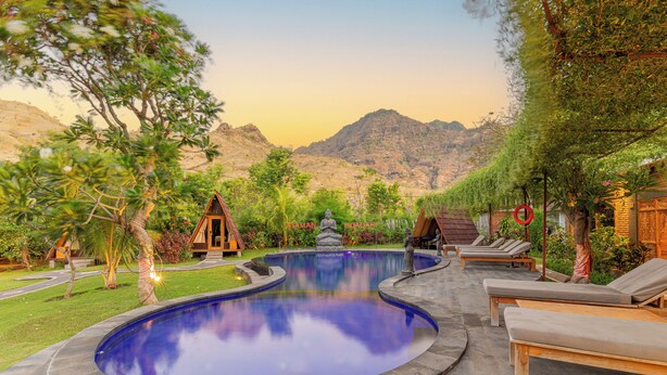 A swimming pool with lounge chairs, surrounded by greenery and a mountain backdrop. - Taman Bidadari Eco & Wellness (Pemuteran)