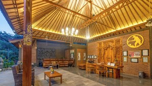 A spacious lounge area with a high ceiling and a thatched roof, furnished with leather sofas and wooden tables. - Taman Bidadari Eco & Wellness (Pemuteran)