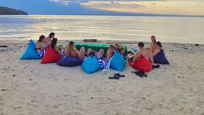 A group of people sitting on bean bags on a sandy beach with a calm sea and a cloudy sky in the background. - Taman Bidadari Eco & Wellness (Pemuteran)