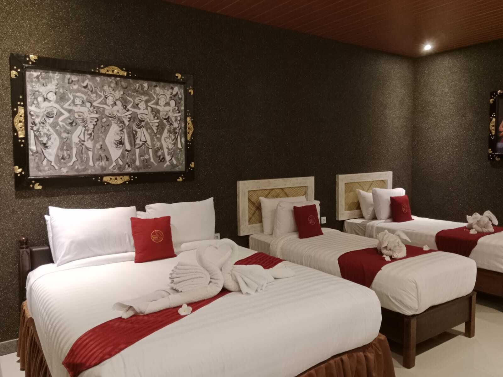 A hotel room with three beds, each with white bedding and red accents. There is a large framed artwork on the wall above the beds.