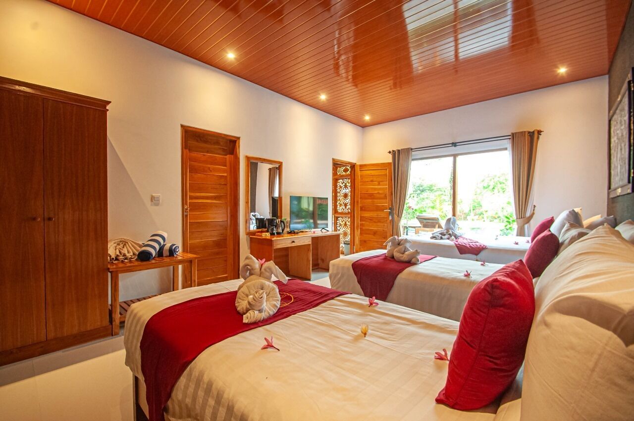 A hotel room with two beds, wooden ceiling, a desk with a chair, a TV, and a window with curtains.