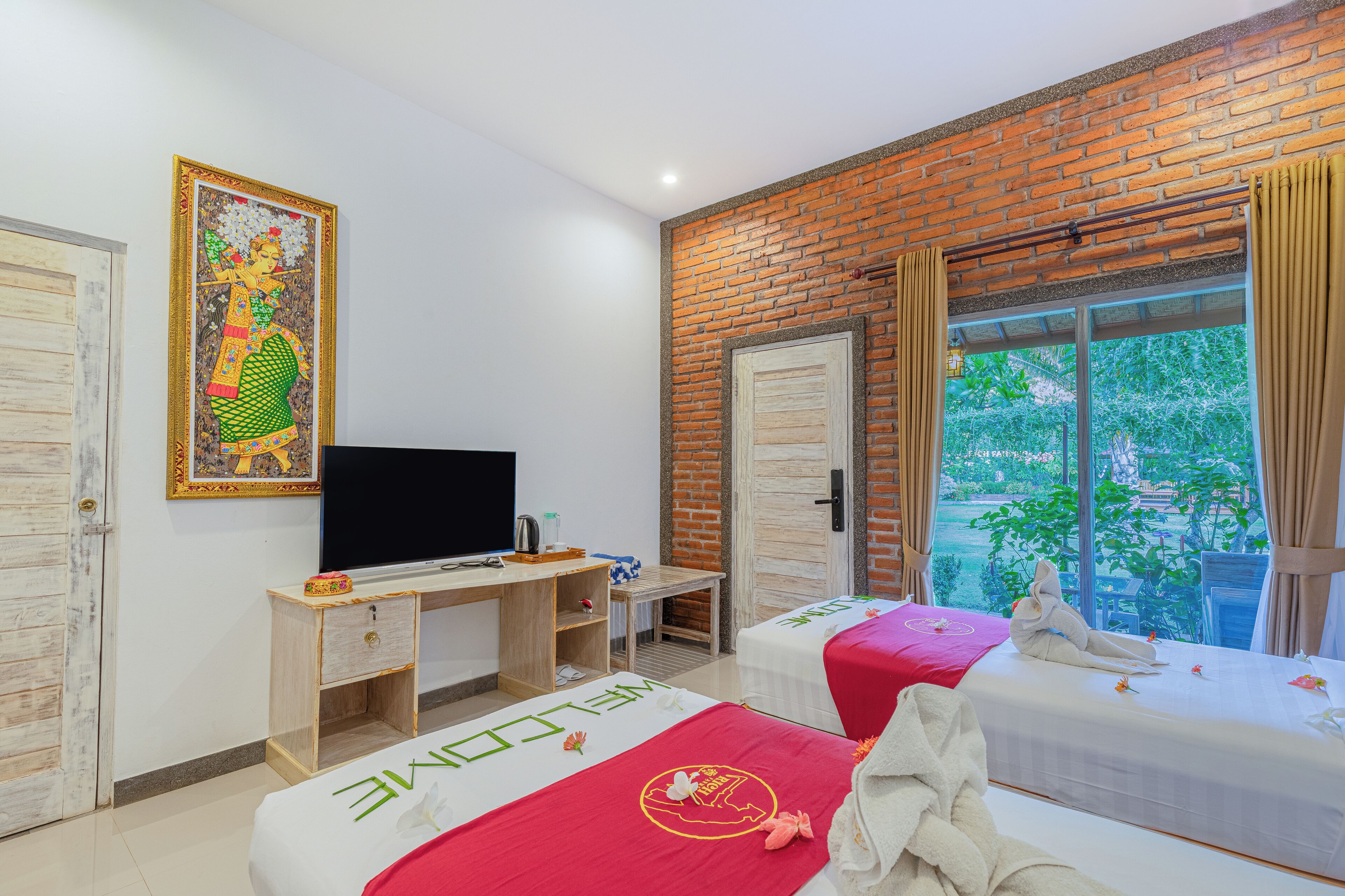 Een kamer met een bakstenen muur, een televisie, twee bedden, een bureau en een raam met uitzicht op groen.