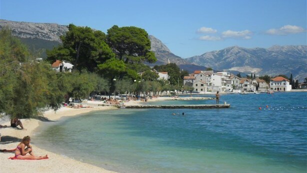 A coastal town with a sandy beach, clear blue waters, and buildings with red roofs. - Baletna Skola (Kastela)