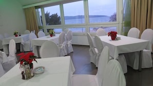 A dining area with tables set for guests, large windows with a view of the water, and white chairs. - Baletna Skola (Kastela)