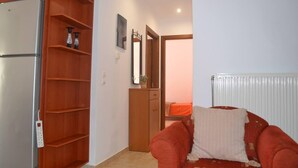 A compact living space with a built-in wooden wardrobe, a small kitchenette with a refrigerator, a red sofa, and a radiator. - Lovely 3-Bed House in Bali (Bali)