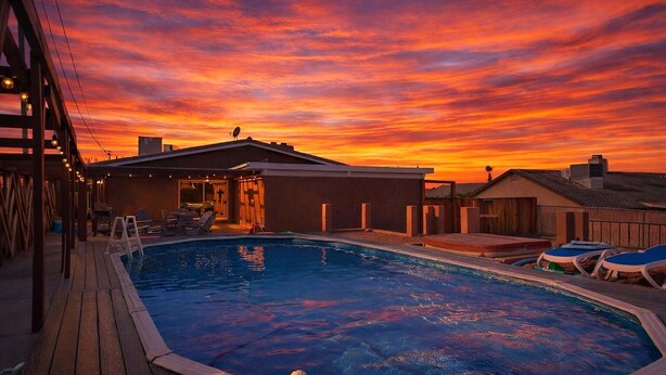 A pool area with a sunset view, a covered seating area, and a building with a sloped roof. - Large Family Retreat Pool Hot Tub Game Room Sauna (Lake Havasu City)