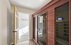 Un couloir avec une porte en bois, une porte en verre dotée d’une poignée, et un téléviseur posé sur une étagère.
