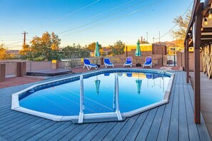 Une piscine dotée d’une terrasse en bois, entourée de chaises longues et de parasols.