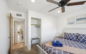 Une chambre à coucher comprenant un lit, un ventilateur de plafond, une table de chevet, une commode, un fauteuil suspendu, une armoire et une porte donnant sur une autre pièce.