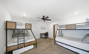 Une chambre avec deux lits superposés, un bureau, une chaise, un ventilateur de plafond et un sol recouvert de moquette.