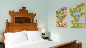 A neatly made bed with a wooden headboard, a bedside table with a lamp, and two abstract paintings on the wall.