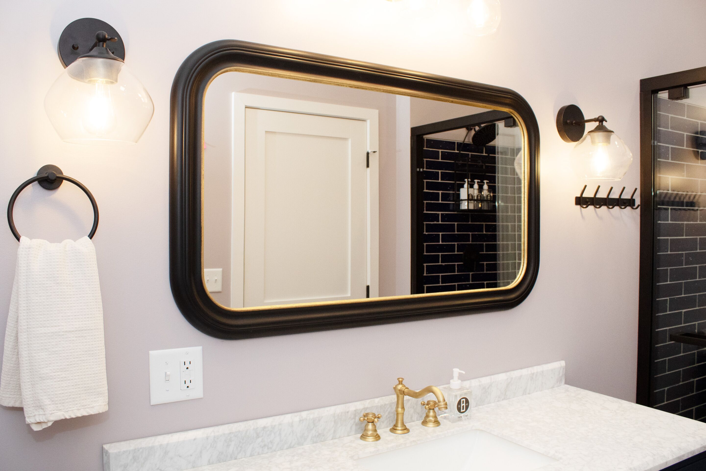 A bathroom with a white marble countertop, a gold faucet, and a large mirror with a black frame.