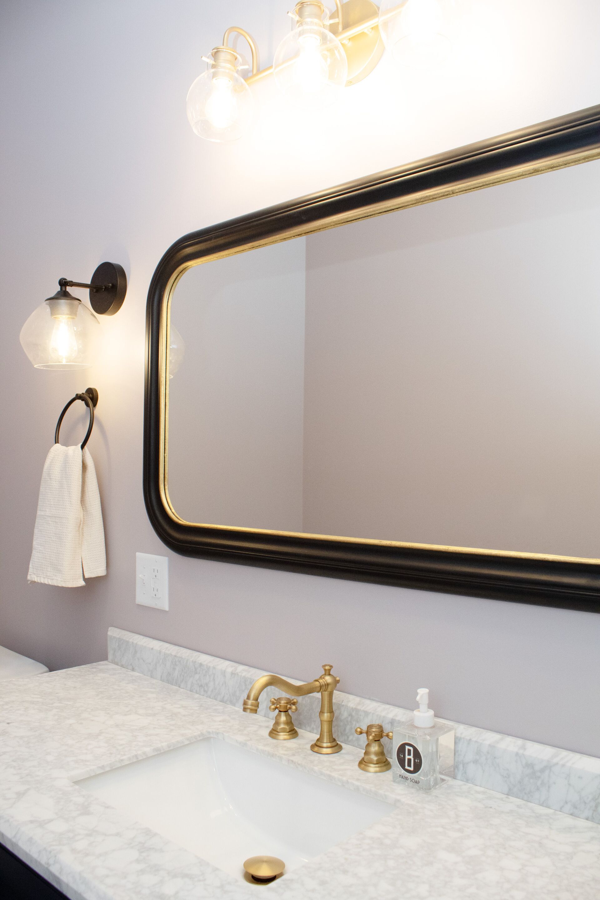 A bathroom with a marble sink, gold faucets, and a large mirror with a gold frame.