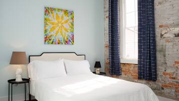 Un dormitorio con cama, mesita de noche, lámpara, un cuadro en la pared y ventana con cortinas.