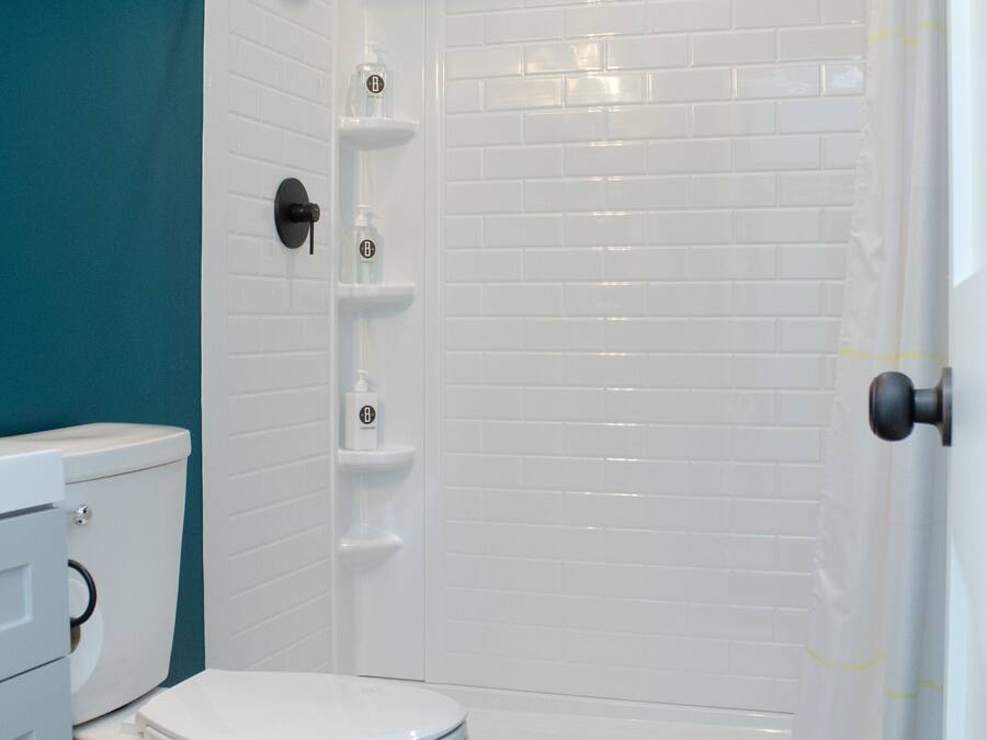 A bathroom with a white toilet, a shower with a white curtain, and a blue trash bin.