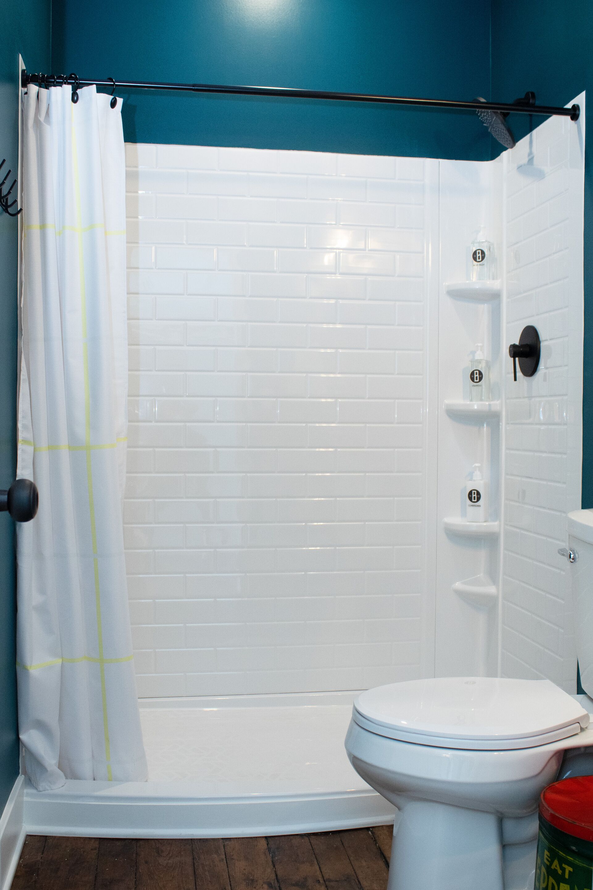 Un baño con inodoro blanco, ducha con cortina blanca y pared de azulejos blancos.