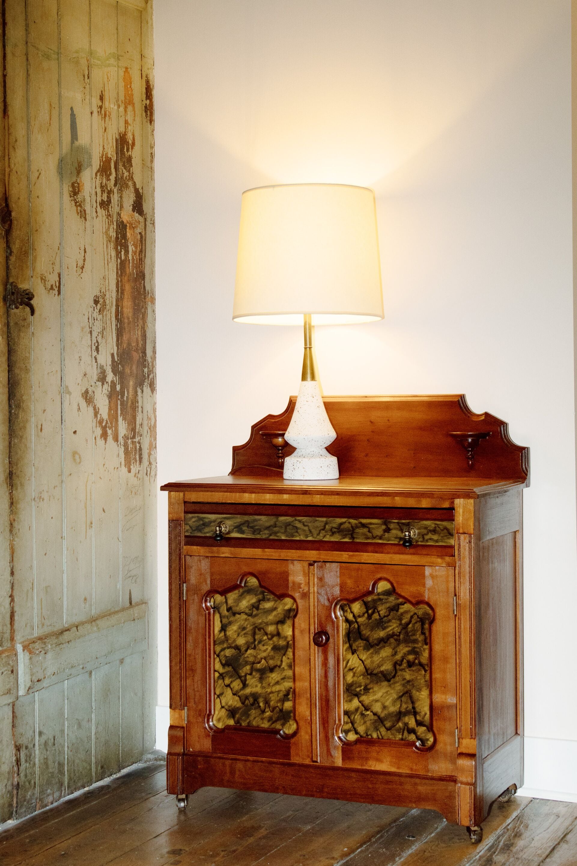 A wooden cabinet with a white lamp on top, positioned against a white wall.