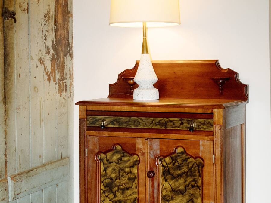 Ein Holzschrank mit einer weißen Lampe darauf, vor einer weißen Wand platziert.