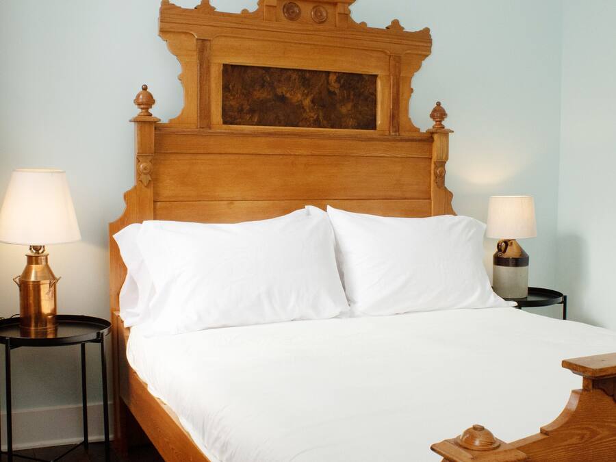 Una cama de madera con ropa de cama blanca, dos mesitas de noche con lámparas y un cabecero de madera.