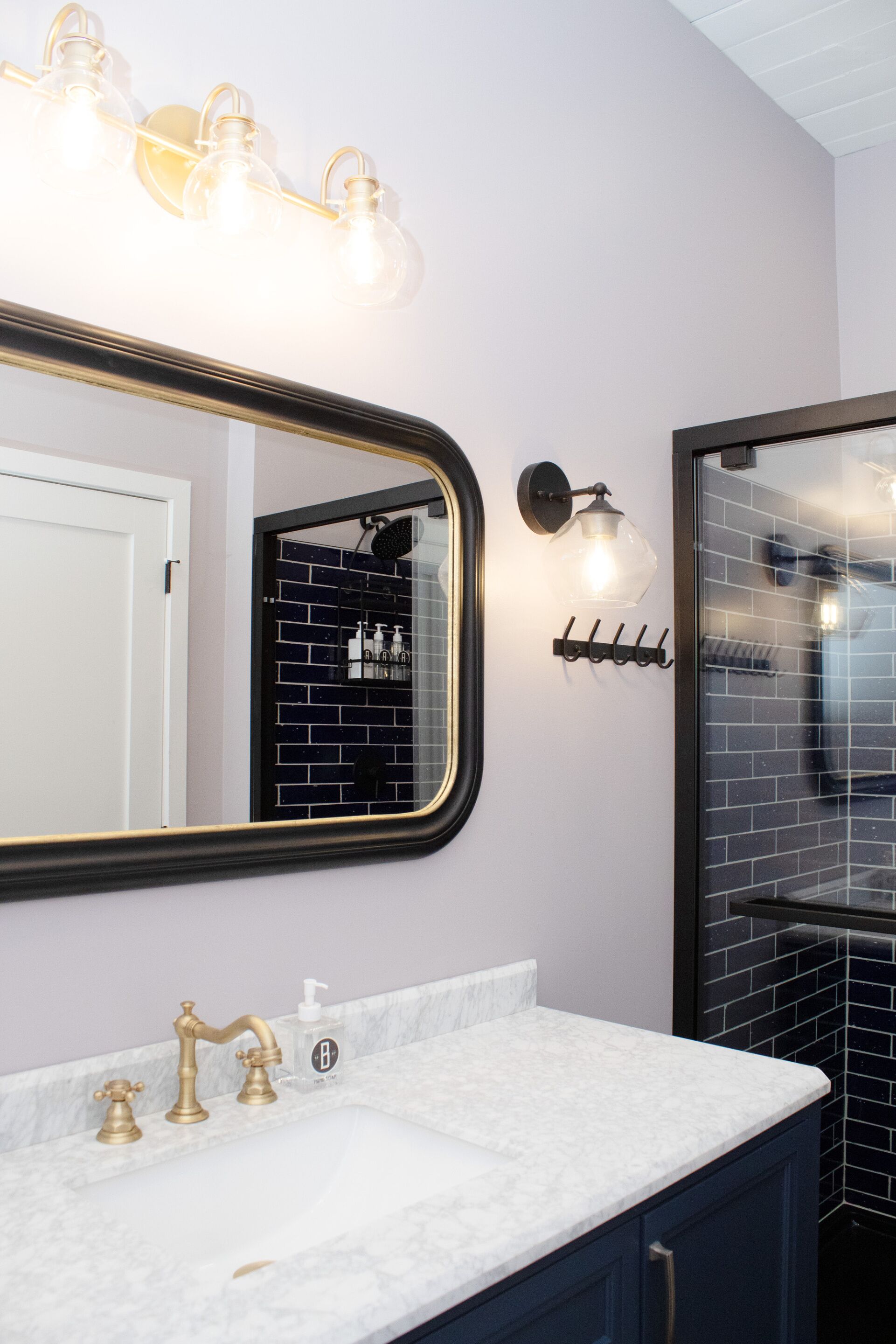 A bathroom with a white marble sink, gold faucets, a large mirror, and black tiled walls.