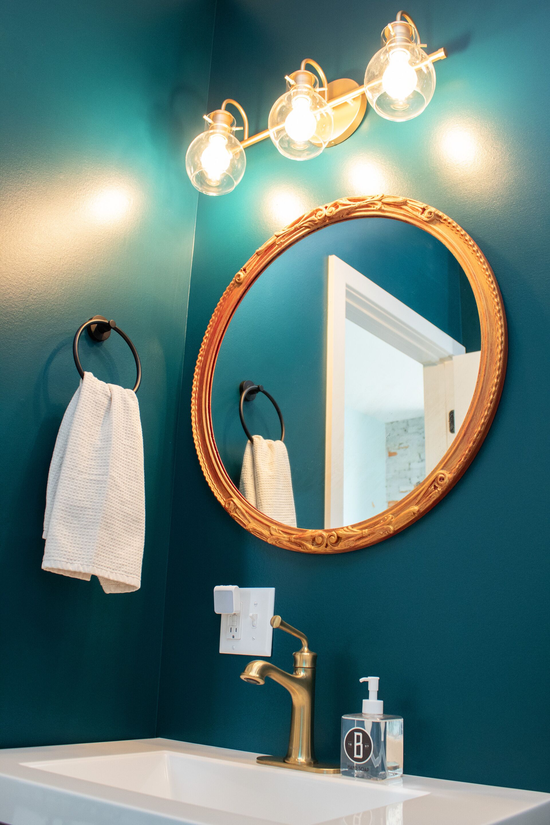 A bathroom with a round mirror, a towel rack, a sink with a faucet, and a hand soap dispenser.