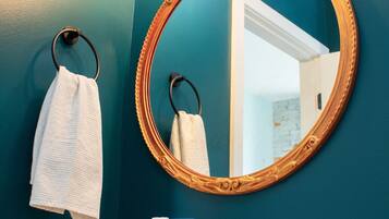 A bathroom with a round mirror, a towel rack, a sink with a faucet, and a hand soap dispenser.