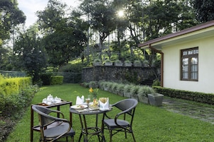 Un espacio de comedor al aire libre con pared de piedra, un edificio pequeño con ventana y césped bien cuidado.
