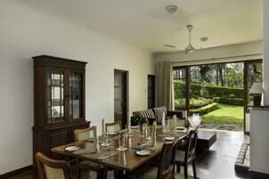 Un comedor con una mesa de madera dispuesta para seis personas, un aparador de madera oscura y vistas a un jardín cuidado a través de amplias ventanas.