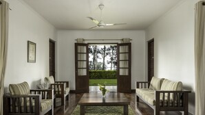 A spacious living room with a large wooden coffee table, two sofas, and a view through open French doors to a garden. - Olive Bungalow - Jetwing Select (Welimada)