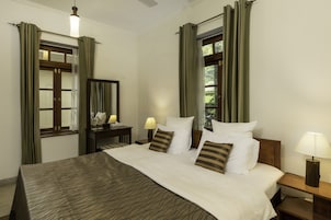 A neatly made bed with a patterned bedspread, a bedside table with a lamp, and a window with curtains.