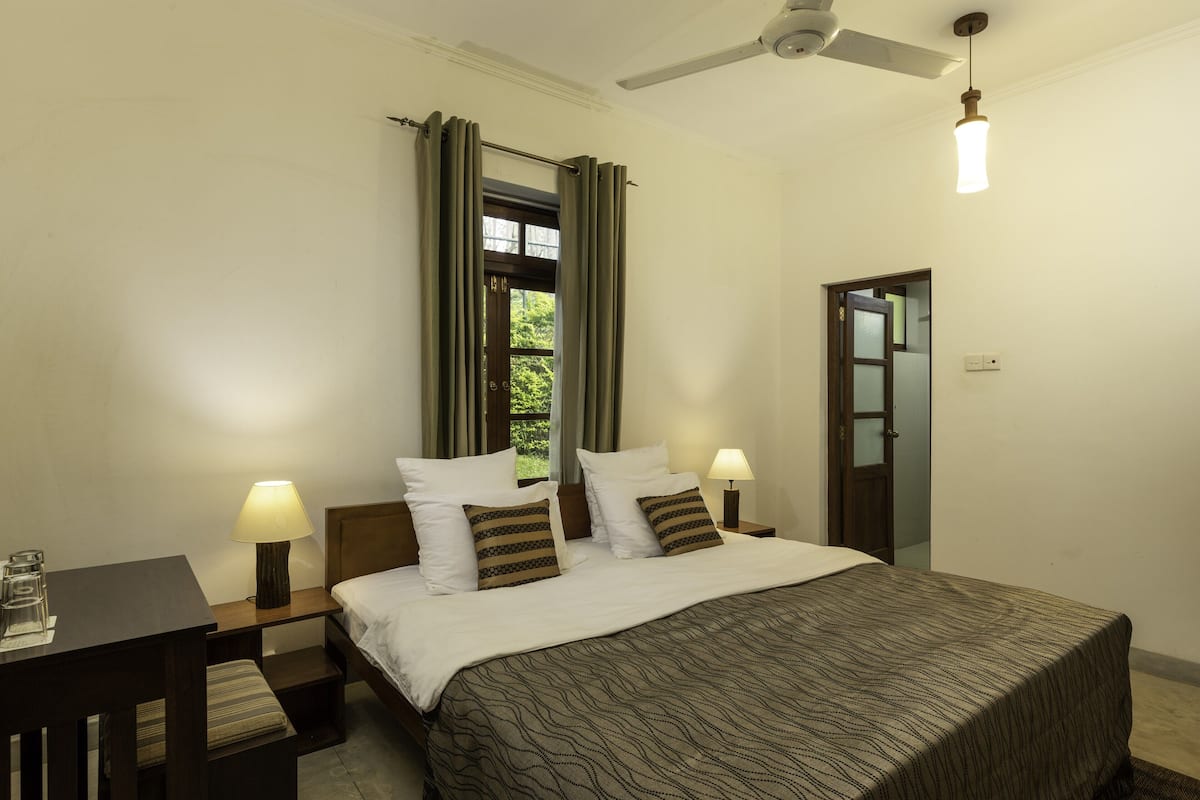 A hotel room with a bed, bedside tables, a desk, and a ceiling fan.