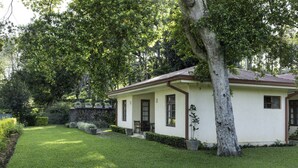 A single-story house with a front porch, a stone wall, and a well-maintained lawn. - Olive Bungalow - Jetwing Select (Welimada)