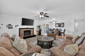 A living room with a fireplace, sofas, a coffee table, a TV, and a ceiling fan.