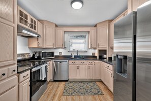 A modern kitchen with wooden cabinets, stainless steel appliances, and a patterned rug. - Luxury Oasis, Hot Tub, Outdoor Kitchen and Grill, Arcade Room, Sleep up to 13 (Fresno)
