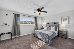 A bedroom with a bed, bedside tables, a ceiling fan, a window with curtains, and a view of the outside. - Luxury Oasis, Hot Tub, Outdoor Kitchen and Grill, Arcade Room, Sleep up to 13 (Fresno)