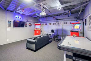 A gaming room with a pool table, a couch, arcade machines, and a neon sign.