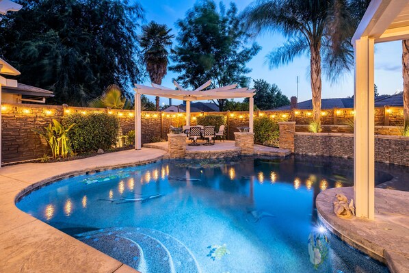A swimming pool with a pergola, stone walls, and string lights.