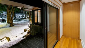 Una habitación con un piso de baldosas, una puerta corrediza que da a un área exterior nevada y otra puerta de madera.