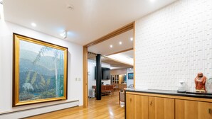 Un interior moderno con un cuadro grande enmarco, suelo de madera y una zona de cocina con armarios y encimera.