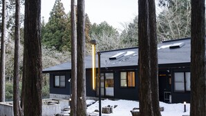 Un edificio moderno rodeado de árboles altos, con una terraza de madera y suelo cubierto de nieve.